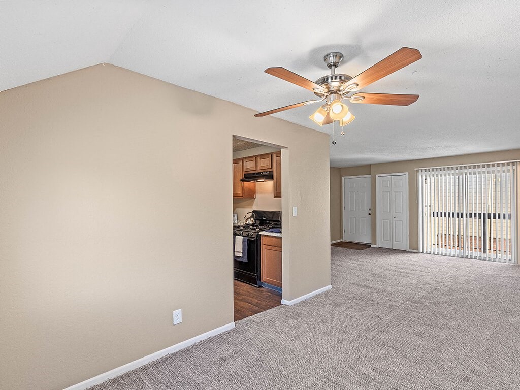 an empty living room with a ceiling fan and a kitchen