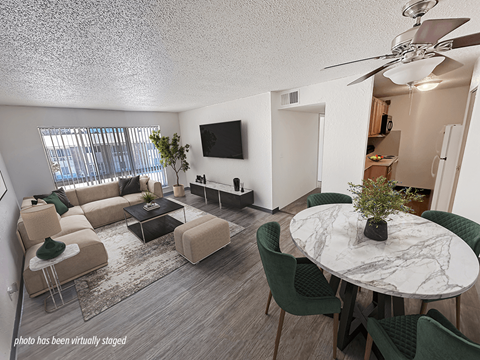 A living room with a white ceiling fan and a white marble table surrounded by green chairs.