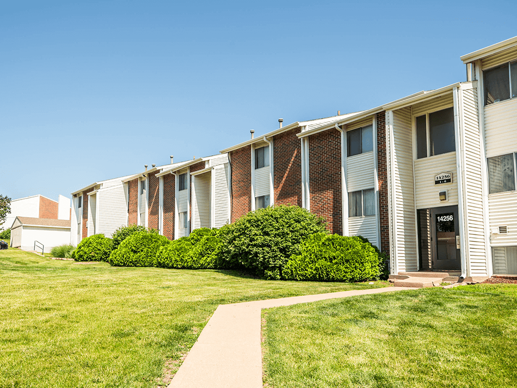 an apartment building with a green lawn and a sidewalk