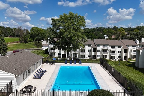 A swimming pool surrounded by a fence and chairs with apartment buildings in the background.