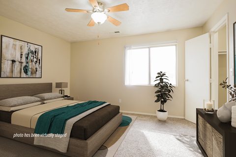 A bedroom with a bed, a ceiling fan, and a plant.