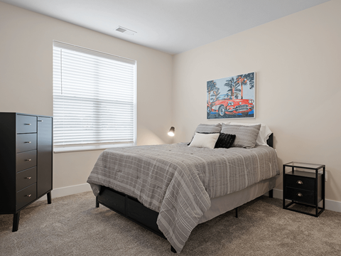 A bedroom with a bed, nightstand, and a painting on the wall.