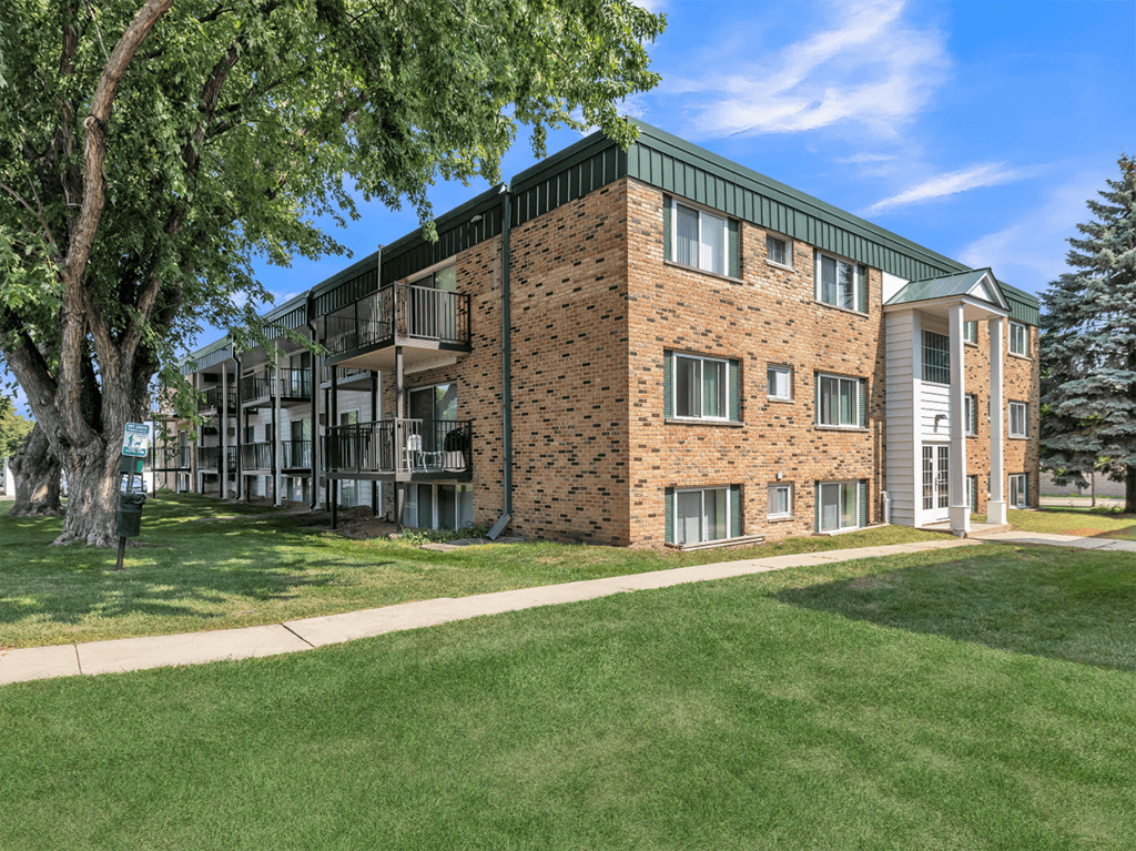 a brick apartment building with green grass and trees