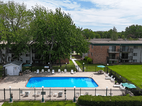 A pool surrounded by lawn chairs and trees.