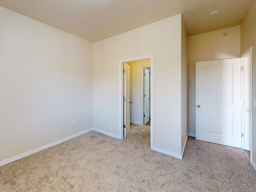 a bedroom with white walls and carpeting and a door to a closet