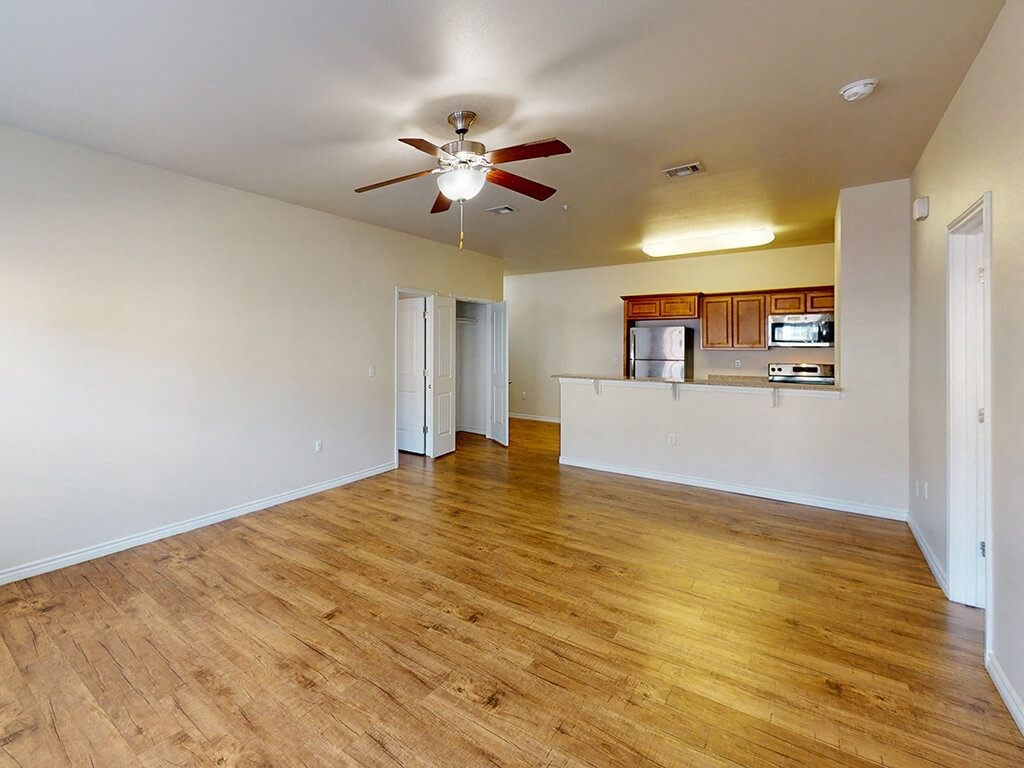 an empty living room and kitchen with a ceiling fan