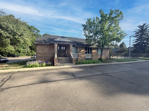 A small house with a black door and windows is surrounded by greenery.