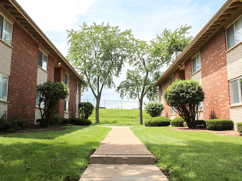 a walkway between two apartment buildings with grass and trees