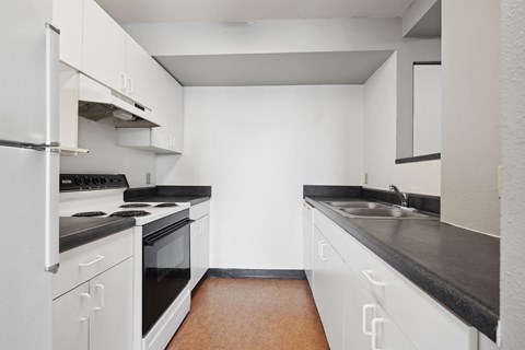 A kitchen with white cabinets and black countertops.