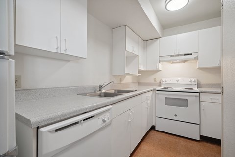 A white kitchen with a sink, stove, and cabinets.