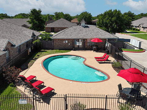 A pool surrounded by a black fence with red chairs and umbrellas.