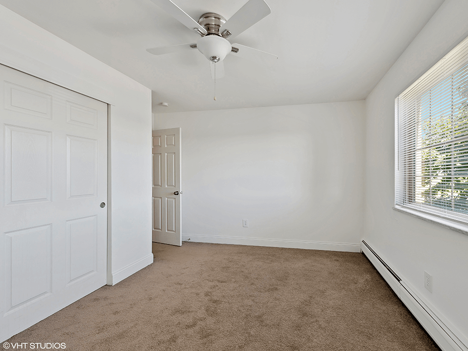 an empty bedroom with white walls and a ceiling fan