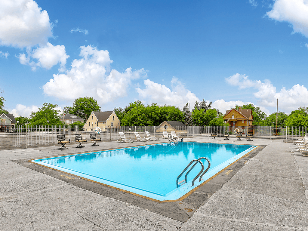 A large outdoor swimming pool surrounded by a fence and lounge chairs.