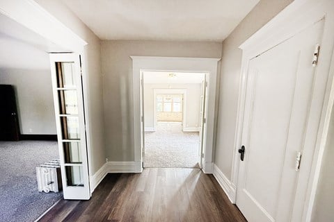 A hallway with a white door and a white cabinet with glass doors.