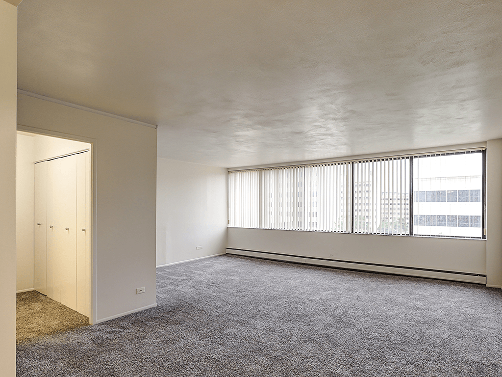 A room with a carpeted floor and a window with blinds.