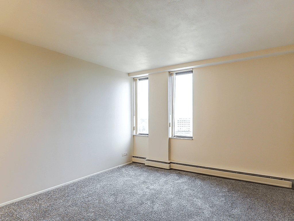 A room with a grey carpet and two windows.