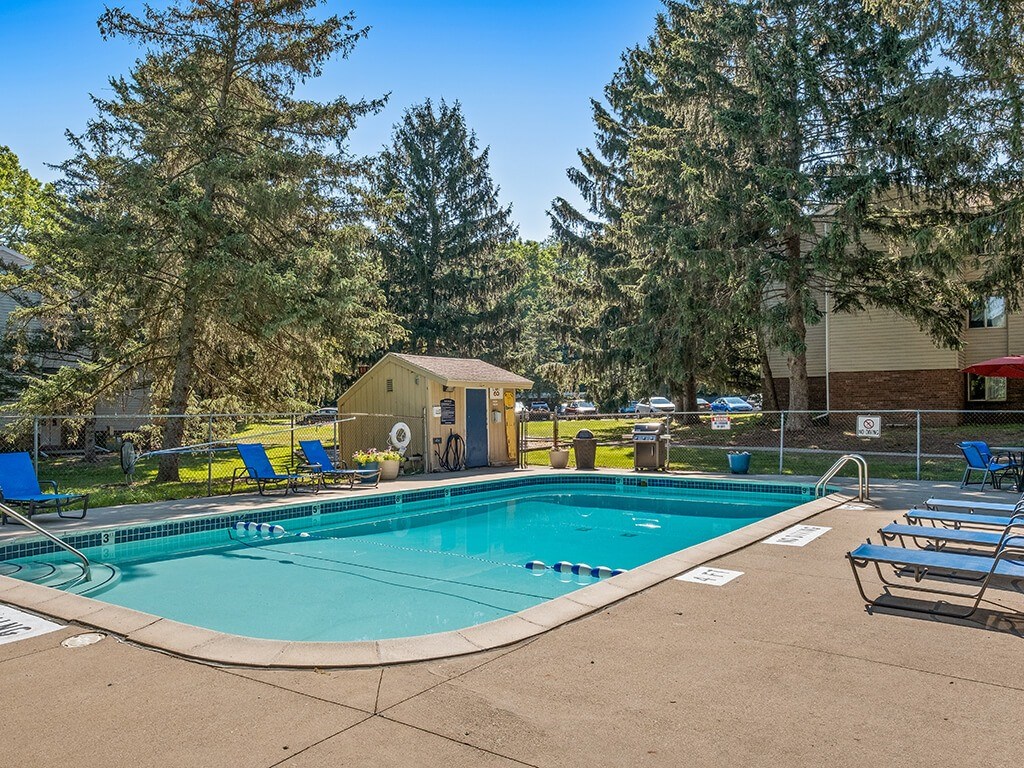 A swimming pool surrounded by trees and chairs.