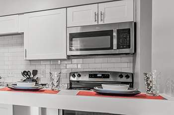 A black and white photo of a kitchen with a microwave, toaster oven, and a red placemat on the counter.