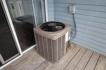 A brown air conditioner unit is on a wooden deck.