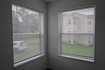A room with two windows, one facing a street and the other a building.