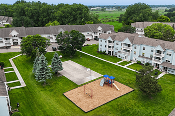 A playground with a blue swing set is surrounded by apartment buildings.