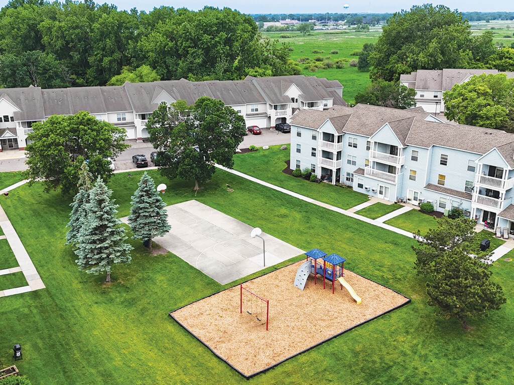 A playground with a slide and a sandbox is surrounded by apartment buildings.
