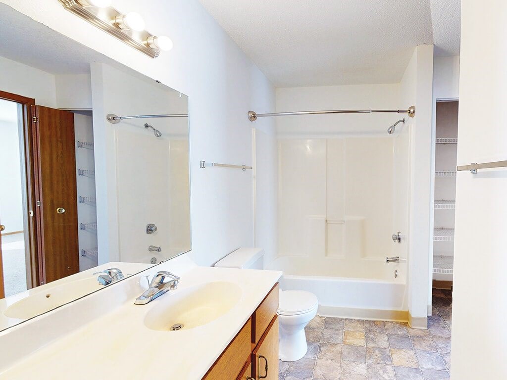 A white bathroom with a double sink and a walk in shower.