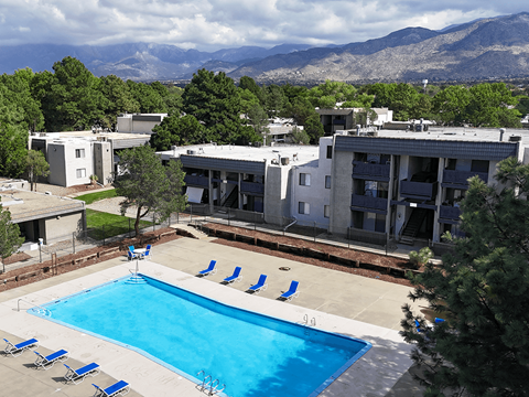 A swimming pool surrounded by chairs and trees with apartment buildings in the background.