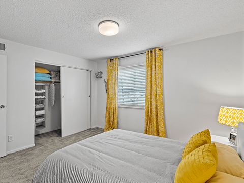 apartment bedroom with a bed and yellow curtains and a closet