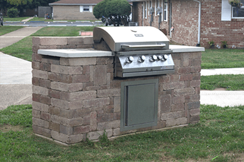 a brick outdoor kitchen with a grill in a yard