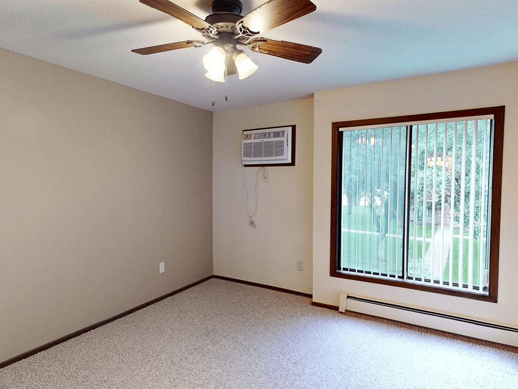 A room with a ceiling fan and a window with a view of trees.