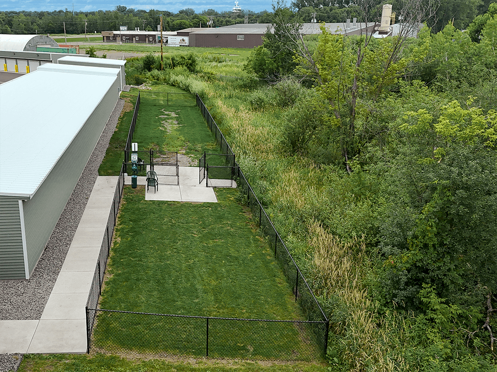 A green fenced dog park area with a small building to the left.