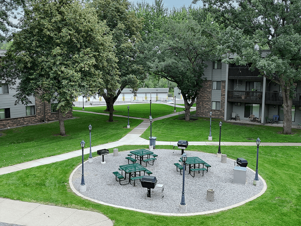 A green picnic area with a table and chairs in the middle of a gravel area.