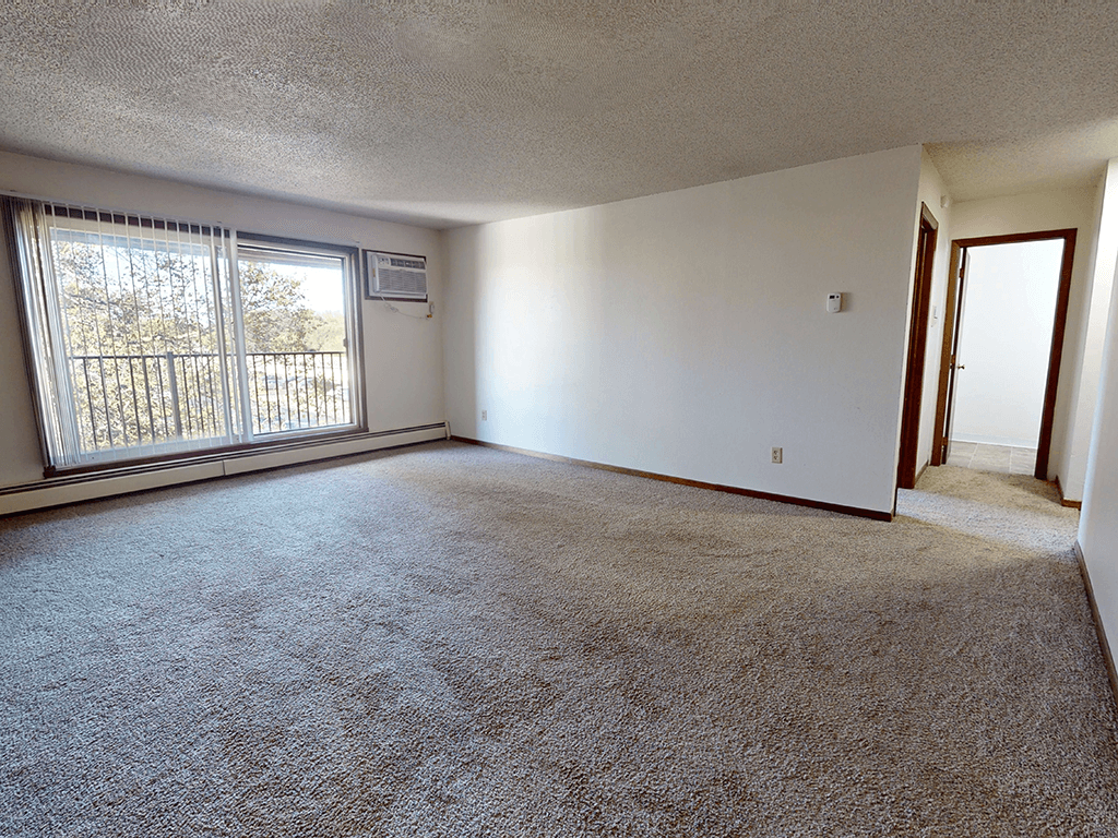 A room with a carpeted floor and a window with blinds.