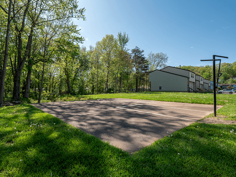 A paved area surrounded by trees and a building in the background.