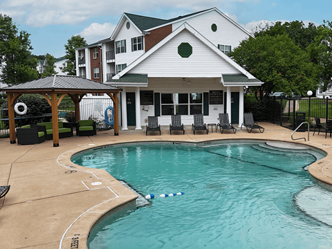 A pool in front of a white building with a gazebo.