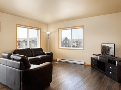 A living room with black leather couches and a wooden floor.
