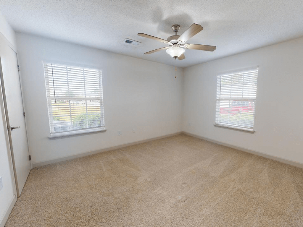 an empty room with a ceiling fan and two windows
