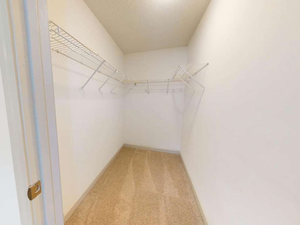 a walk in closet with a white wall and empty shelves