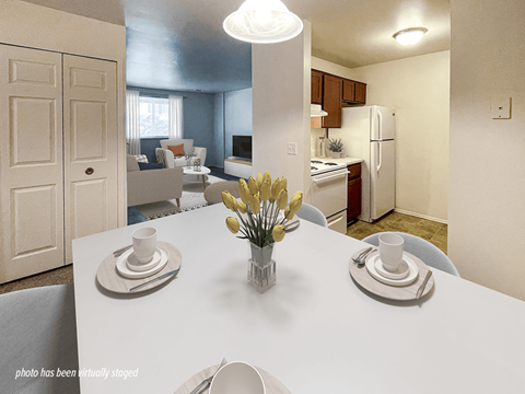 A dining room with a table set for two and a kitchen in the background.
