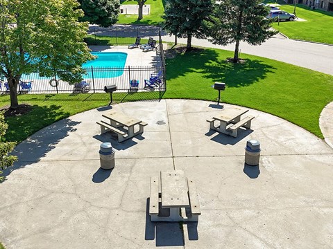 A concrete patio with four benches and a pool in the background.