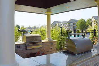 A grill is on a patio with a brick column and a grill cover.