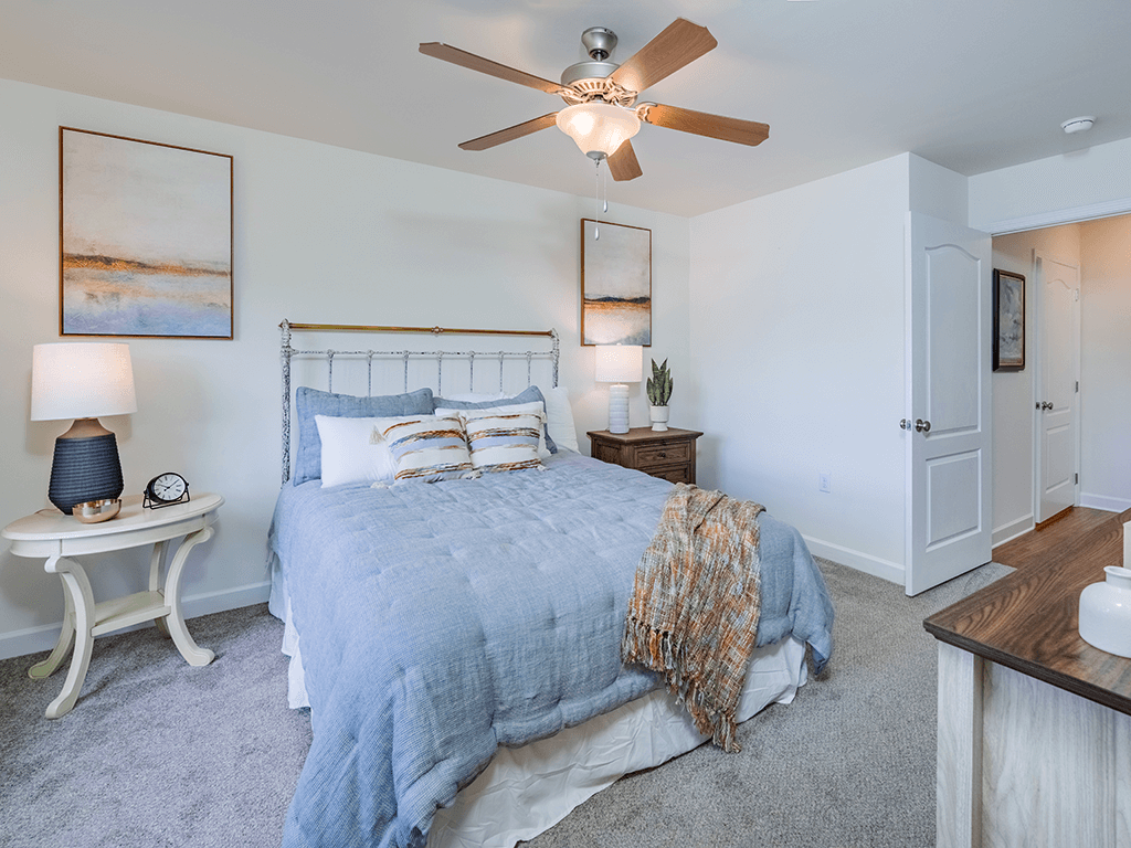 A bedroom with a bed, a fan, and a nightstand.