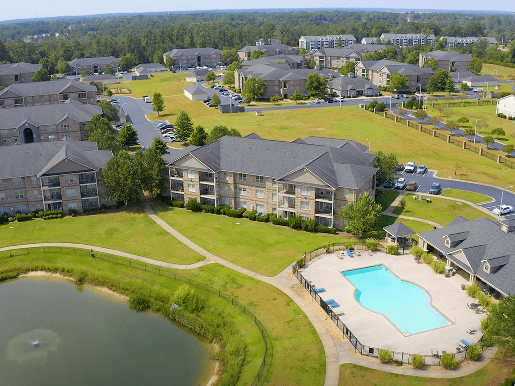 A bird's eye view of a residential area with houses, a swimming pool, and a pond.