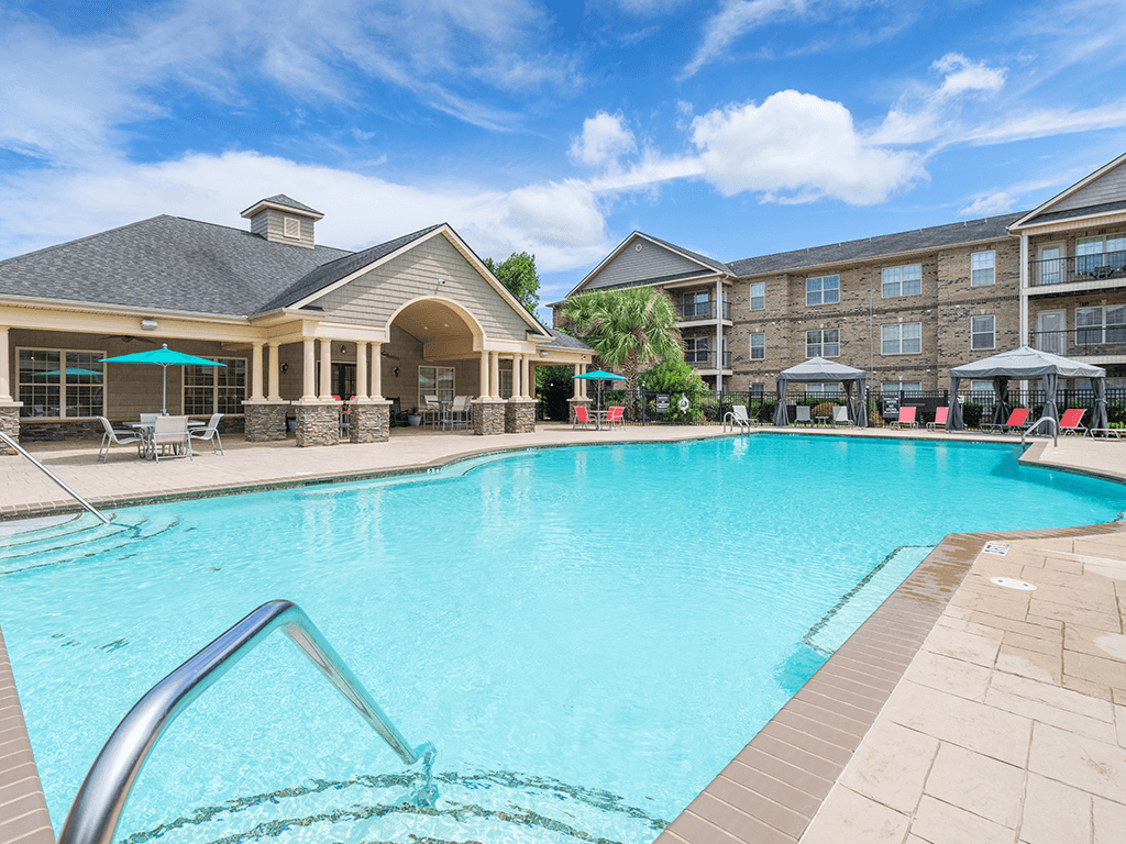 A large swimming pool in front of a building with a patio area.