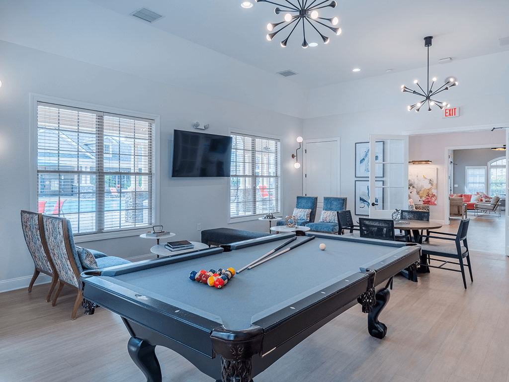 A pool table is in the middle of a room with a television and chairs.
