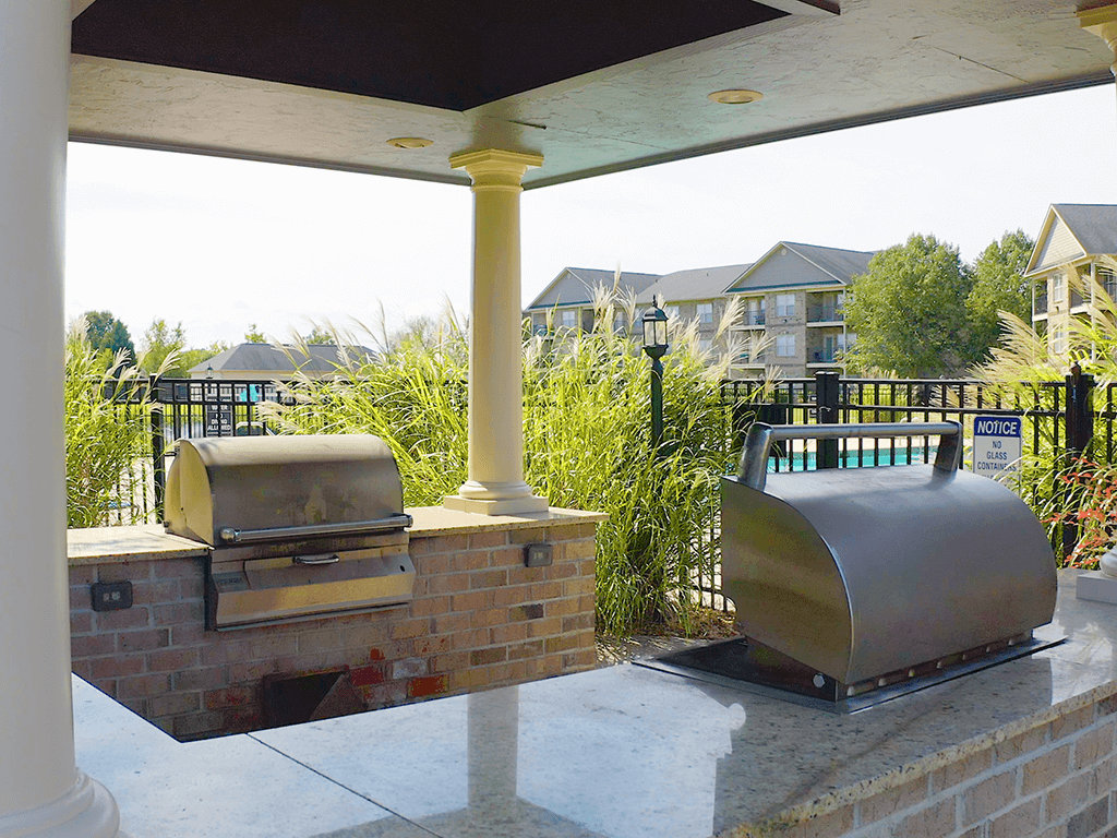 A BBQ grill is on a patio with a notice sign on the fence.
