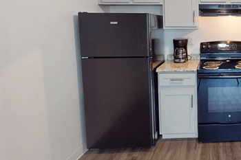 A black refrigerator is in a kitchen with a white oven and stove.