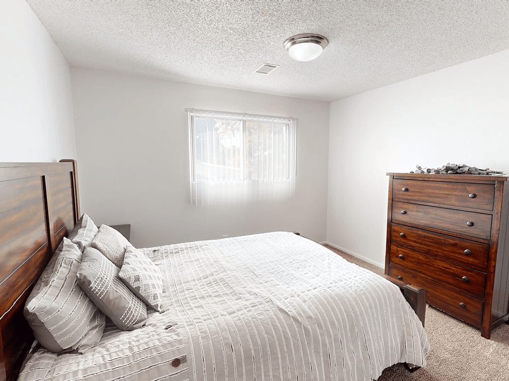 A bedroom with a bed, dresser, and window.