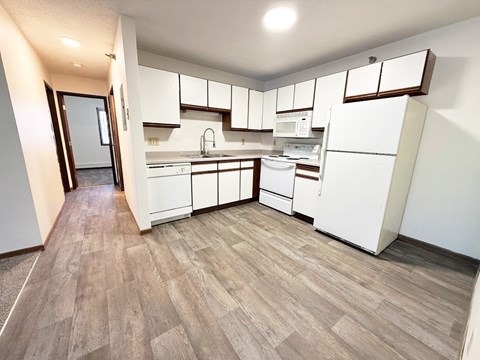 A kitchen with white appliances and wooden floors.